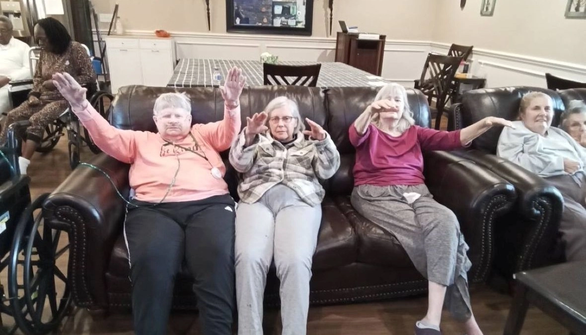 Senior residents sitting on a couch raising their hands in a senior care community