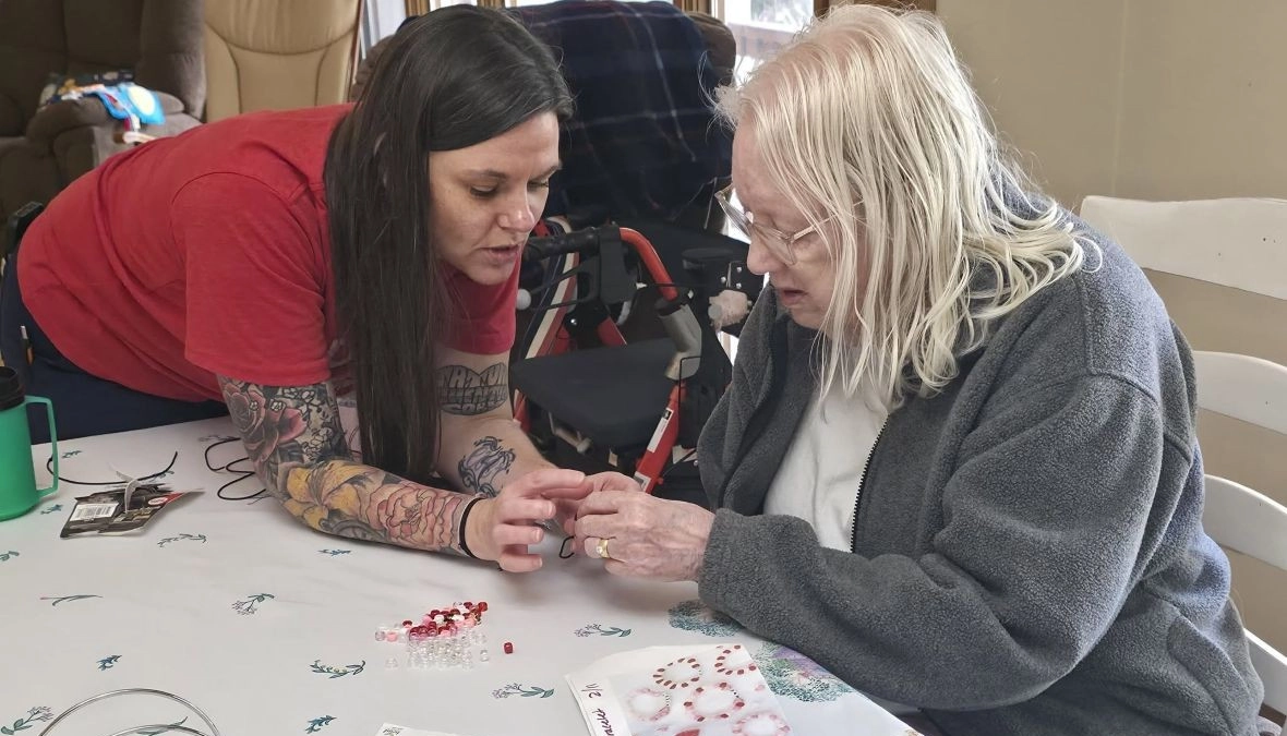 Caregiver assisting an elderly woman with a craft activity at a senior care community