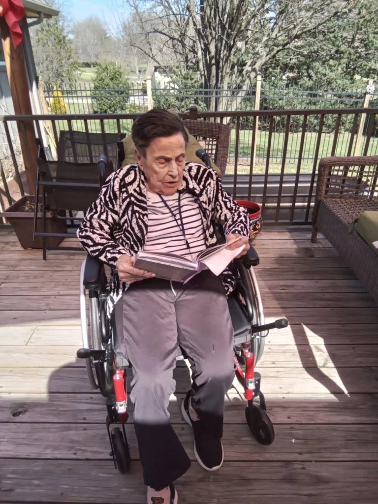 Senior resident in a wheelchair reading a book outdoors in a peaceful senior care community