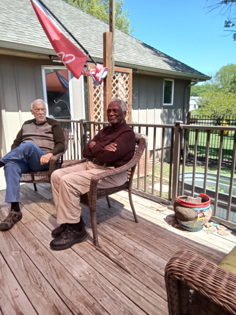Two senior residents relaxing together on an outdoor deck at a senior care community
